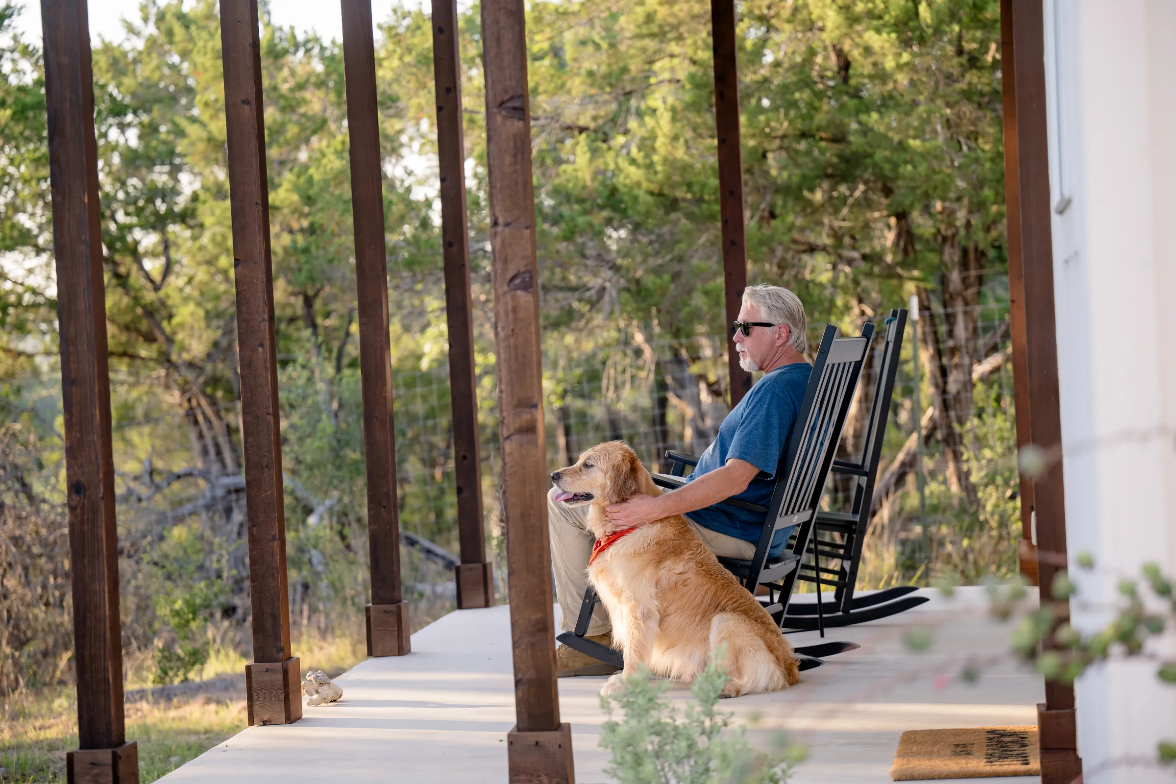 Guest relaxing in a rocking chair with a golden retriever on the Jackrabbit Cottage porch