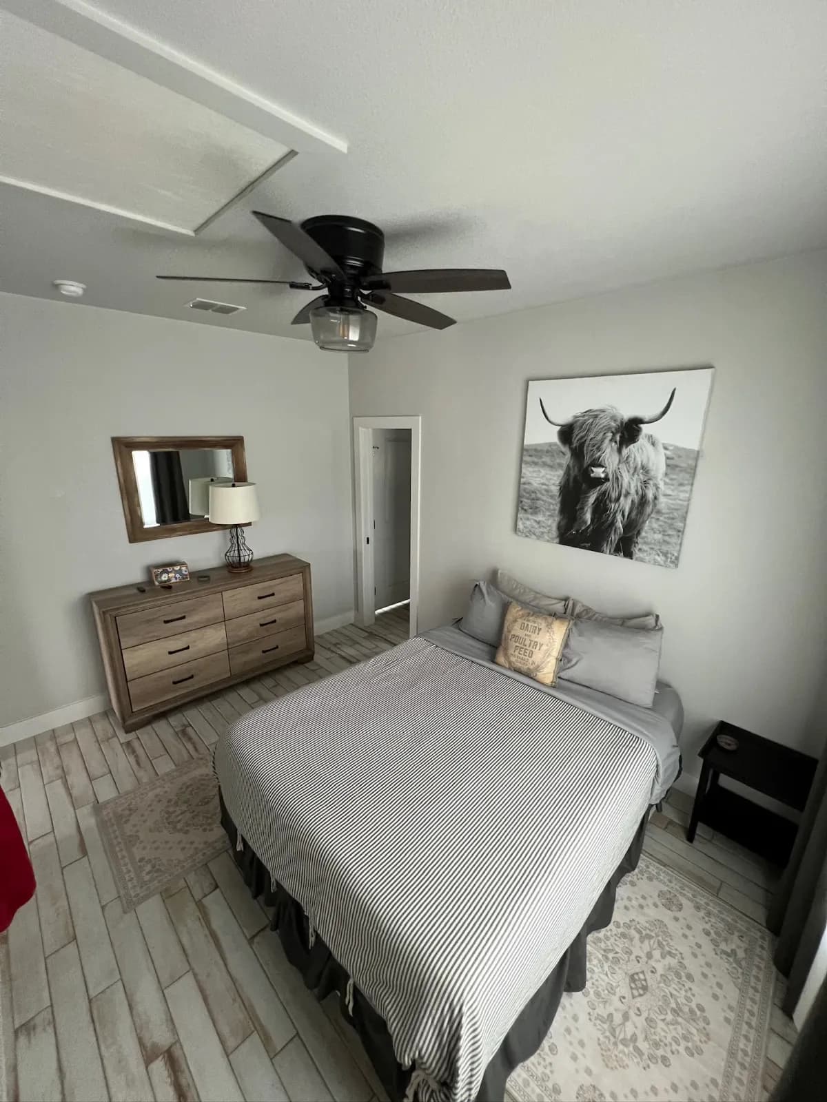 Bedroom with Highland cattle art, striped bedding, and wood dresser inside Summermoon Cottage