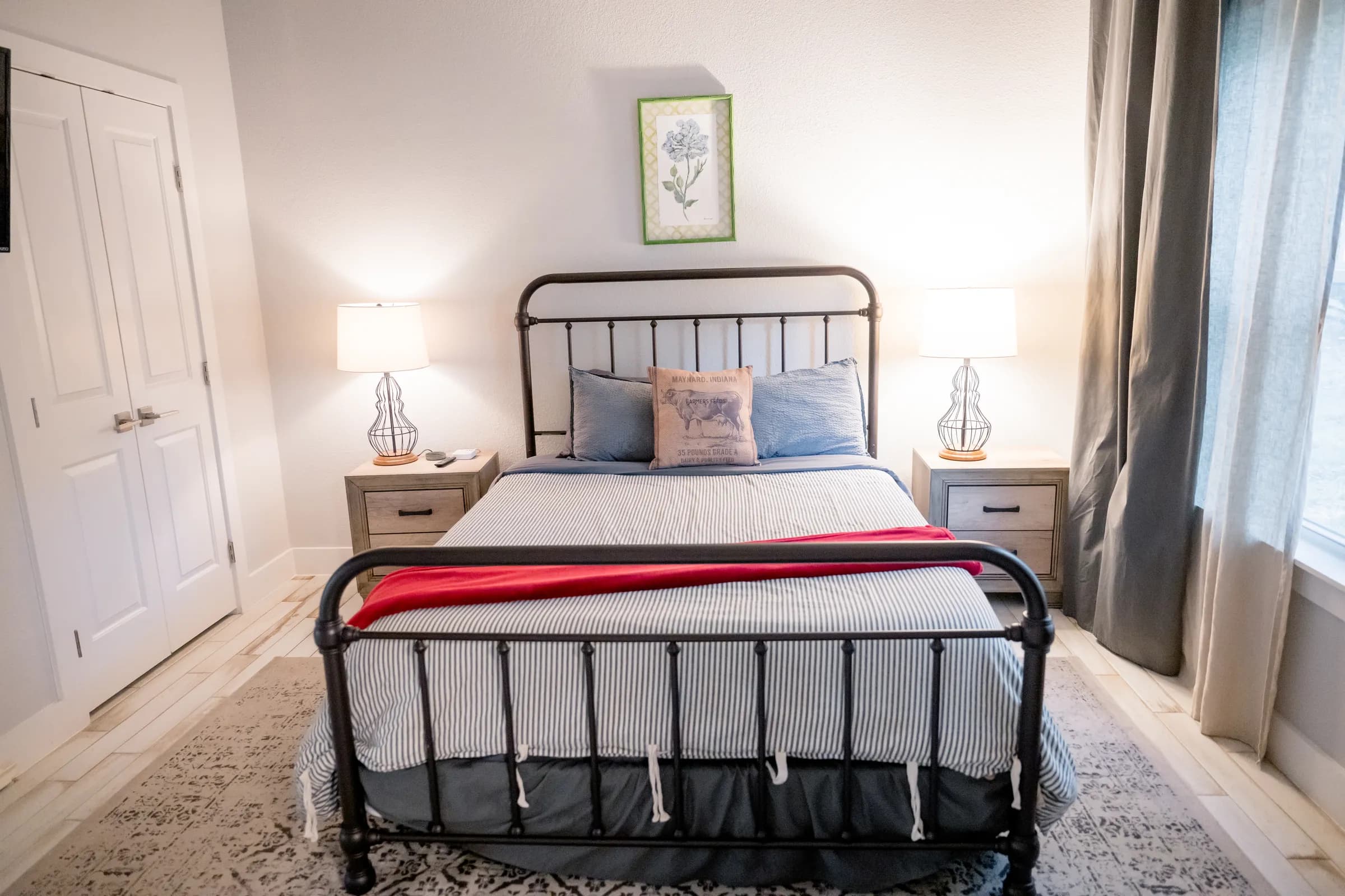 Bedroom with iron bed frame, striped bedding, and red throw inside a Wayside Wimberley farmhouse cottage