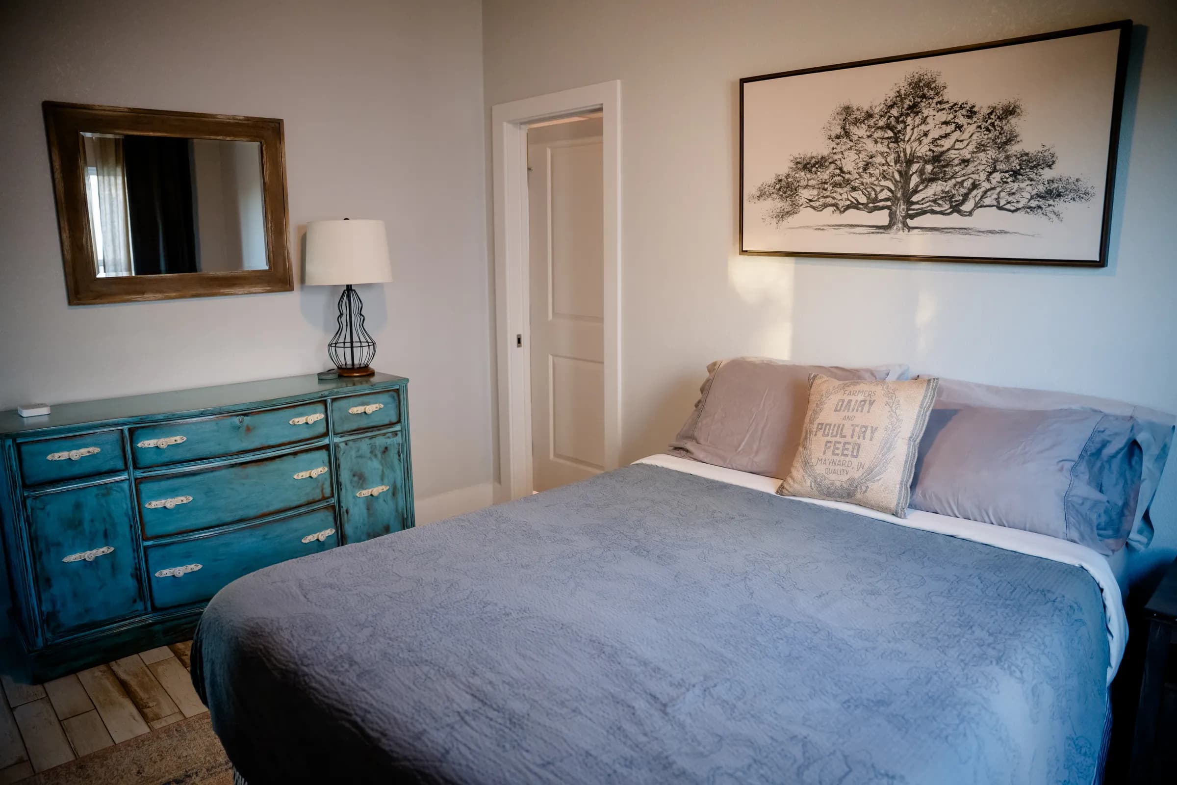 Bedroom with teal dresser, mirror, and oak tree wall art inside a Wayside Wimberley farmhouse cottage
