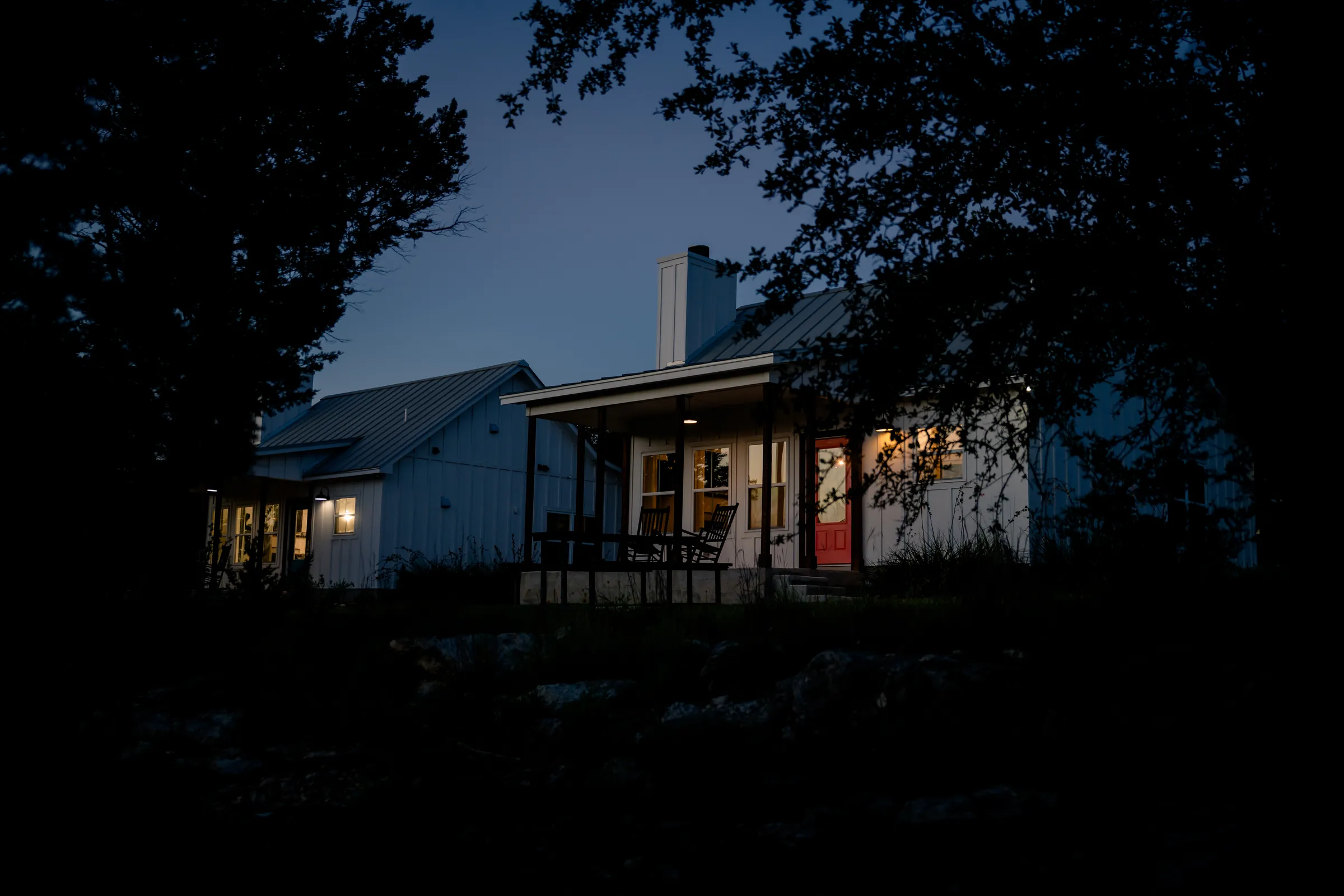 Wayside Wimberley farmhouse cottage exterior at dusk with red front door and porch lights