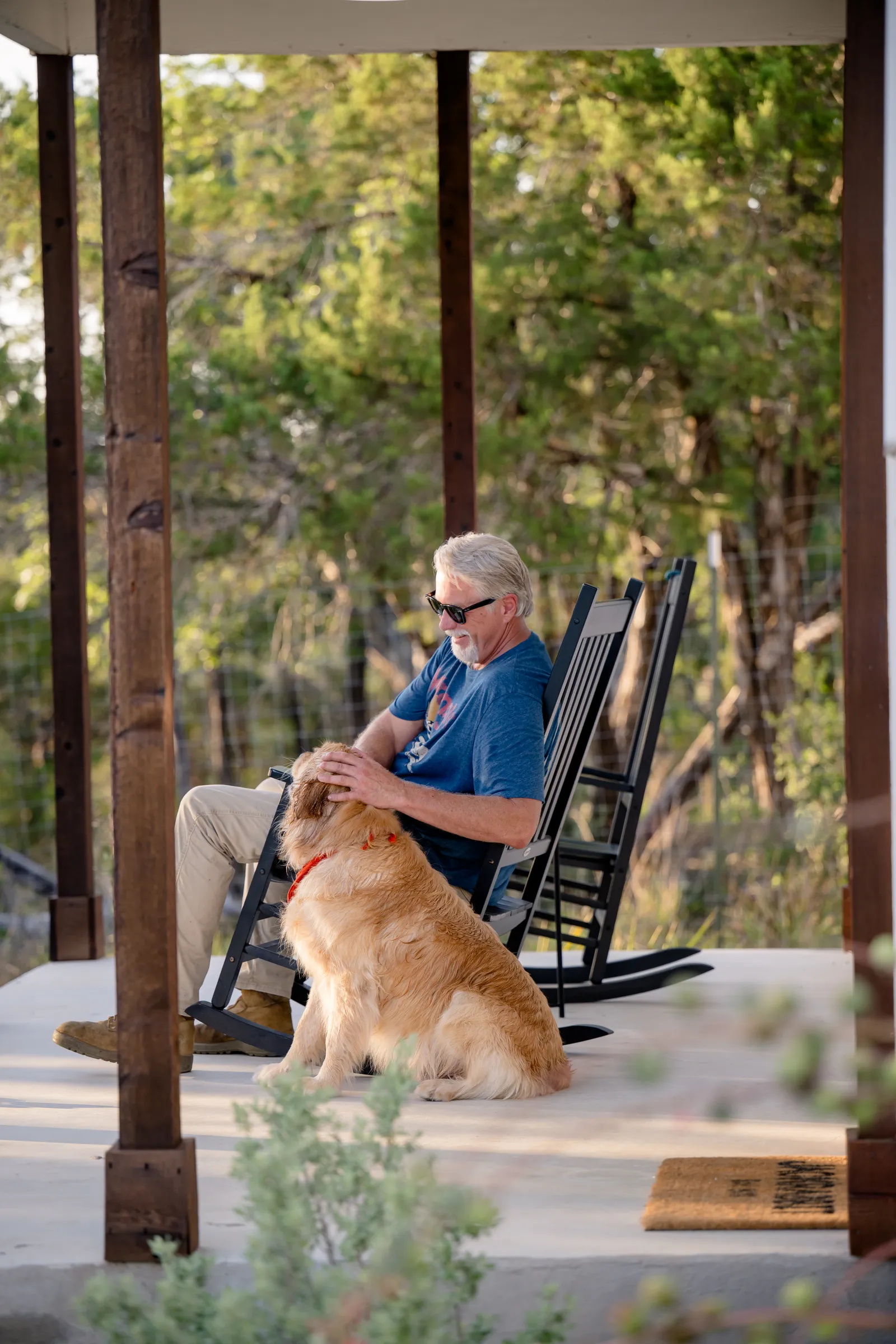 Guest in a rocking chair with a golden retriever on a cottage porch at Wayside Wimberley